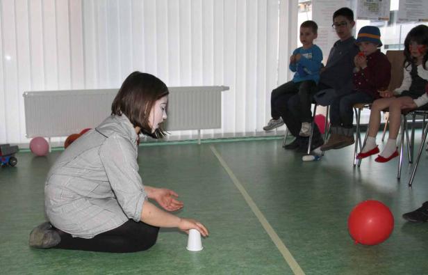 Eine Frau mit Gesichtsbemalung führt einen Becherstapel-Trick vor einer Gruppe von Kindern auf.