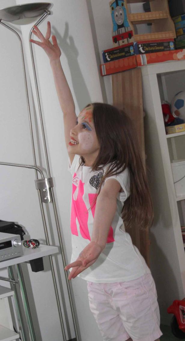 Ein Mädchen mit Gesichtsbemalung versucht, eine Stehlampe zu erreichen.