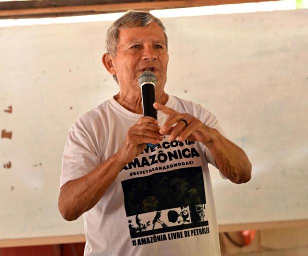 Älterer Mann spricht mit Mikrofon und trägt ein T-Shirt mit Amazonas-Schutzbotschaft.