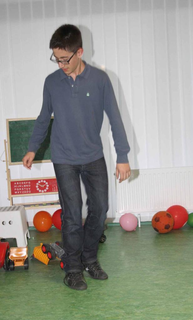 Ein junger Mann mit Brille steht in einem Raum mit Spielsachen und Ballons.
