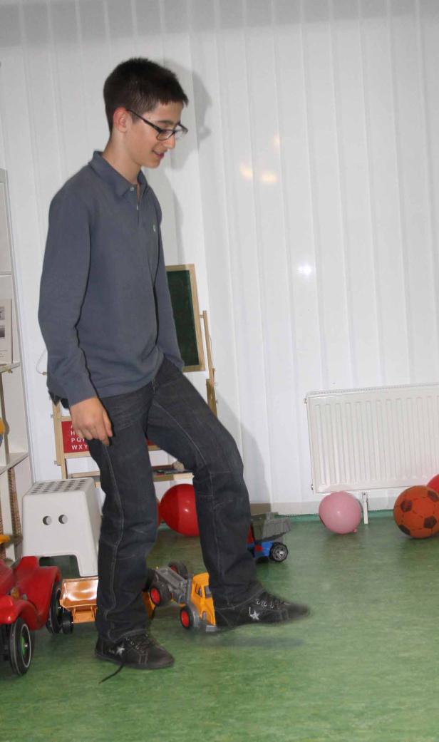 Ein Jugendlicher mit Brille balanciert auf einem Spielzeug-LKW.