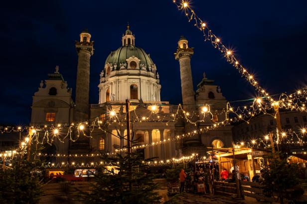 Abendstimmung vor der Karlskirche in Wien mit Weihnachtsbeleuchtung und Christkindlmarktstände.
