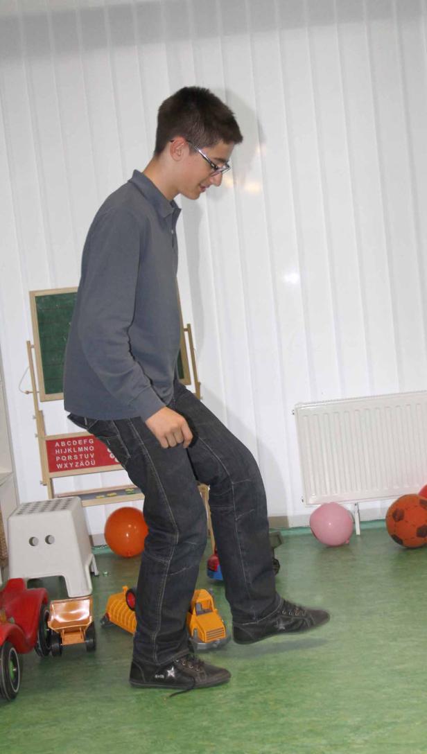 Ein junger Mann mit Brille balanciert einen Ball mit dem Fuß inmitten von Spielzeug.