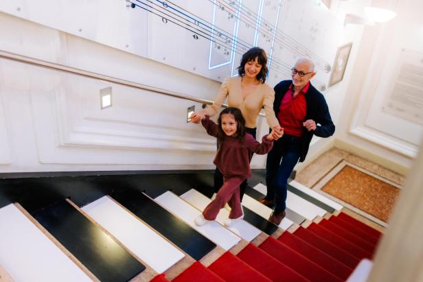 Drei Personen gehen eine Treppe hinauf, deren Stufen aussehen wie die Tasten eines Klaviers.