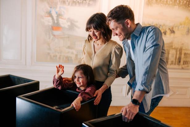 Eine Familie mit einem kleinen Kind befindet sich in einem Museum und spielen ein Spiel mit einem Holzkasten.