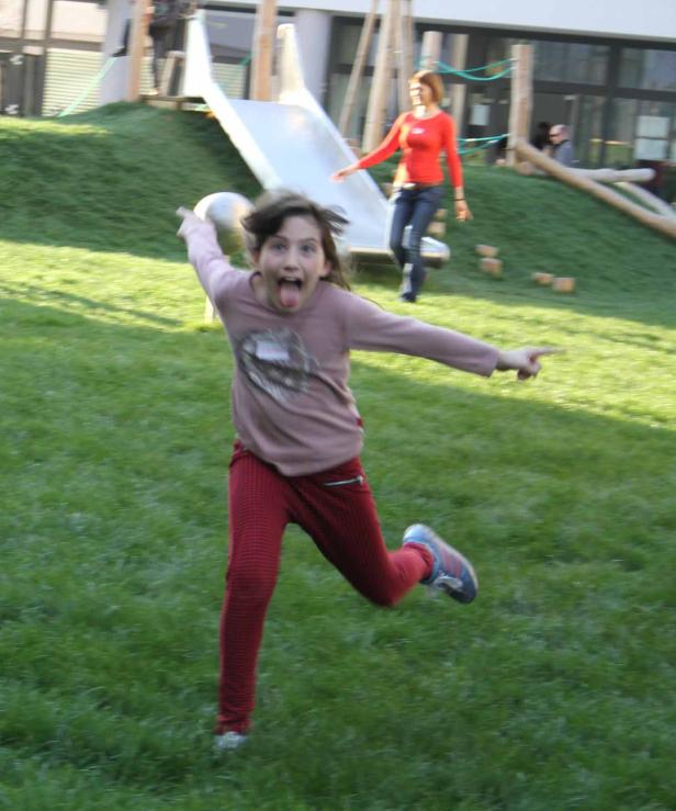 Ein Mädchen rennt auf einer Wiese und streckt die Zunge heraus.