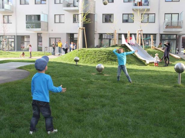 Kinder spielen auf einem Spielplatz mit Rutsche und grüner Rasenfläche.