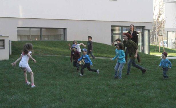 Eine Gruppe Kinder spielt auf einer Wiese vor einem Gebäude.