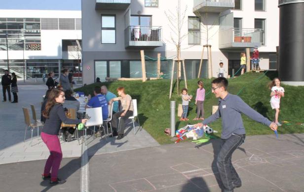 Eine Gruppe von Menschen und Kindern verbringt Zeit im Freien vor einem modernen Gebäude.