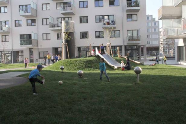 Kinder spielen auf einem Spielplatz vor einem modernen Wohngebäude.