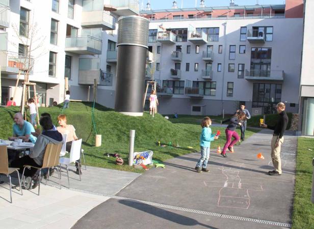 Auf einem begrünten Innenhof spielen Kinder, während Erwachsene an Tischen sitzen.