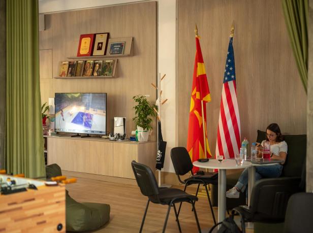 Eine junge Frau sitzt auf einem grünen Sitzmöbel in einem großen Raum und schaut auf ihr Handy.