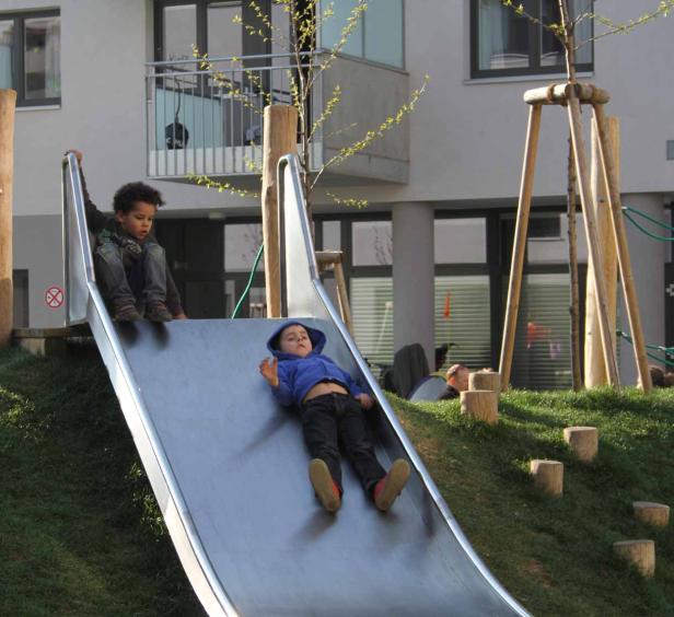 Zwei Kinder spielen auf einer Rutsche auf einem Spielplatz.