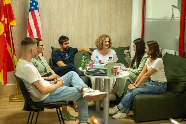 Sechs Menschen sitzen um einen kleinen weißen Tisch herum und reden.