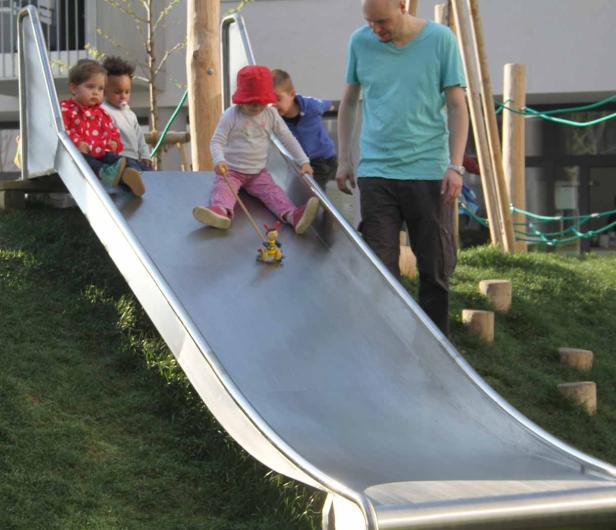 Eine Gruppe von Kindern spielt mit einem Erwachsenen auf einer Rutsche.