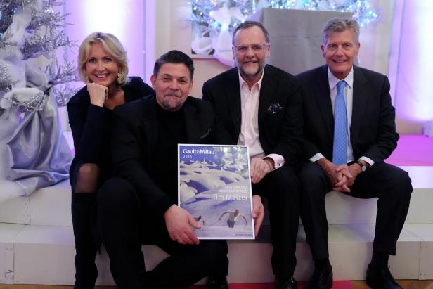 Vier Personen sitzen festlich gekleidet zusammen, eine hält eine Gault&Millau-Urkunde.