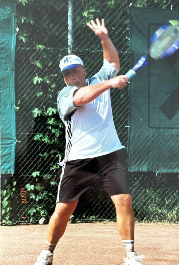 Ein Mann mit Kappe schlägt auf einem Sandplatz mit einem Tennisschläger einen Ball.