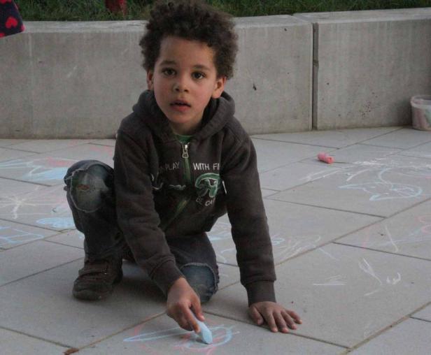 Ein Junge mit lockigem Haar malt mit Kreide auf dem Boden.