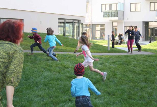 Eine Gruppe Kinder rennt auf einer Wiese vor einem Wohngebäude.