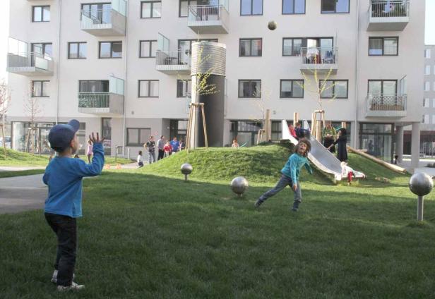 Kinder spielen auf einem Spielplatz vor einem Wohnhaus.