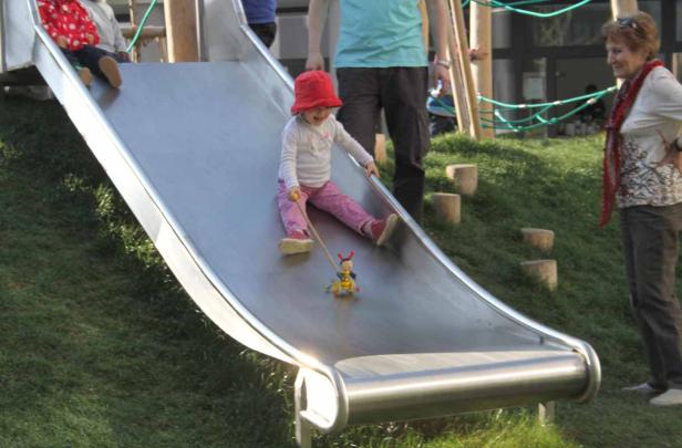 Ein kleines Mädchen rutscht mit einem Spielzeug auf einer Rutsche.