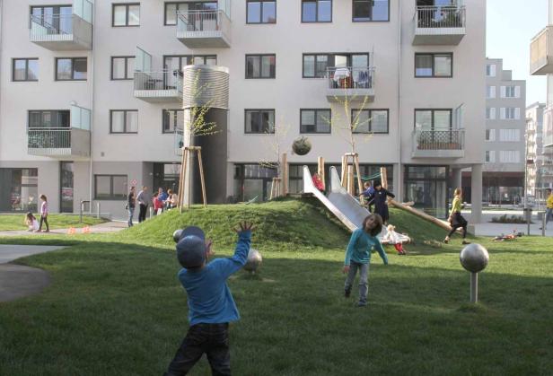 Kinder spielen auf einem Spielplatz vor einem Wohnhaus.