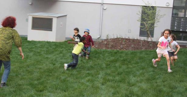 Eine Gruppe Kinder spielt auf einer Rasenfläche vor einem Gebäude.