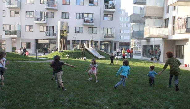 Kinder spielen auf einer Wiese vor modernen Wohnhäusern.