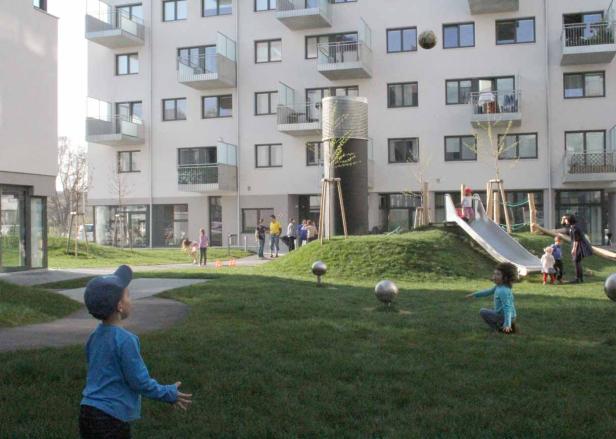 Kinder spielen auf einem Spielplatz vor einem modernen Wohngebäude.