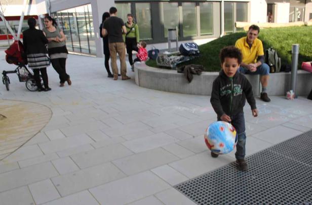 Ein kleiner Junge spielt mit einem Globus-Ball auf einem Platz, während andere Leute im Hintergrund stehen.