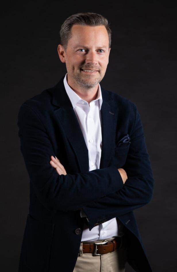 Mann mit weißem Hemd und Sakko grinst in die kamera