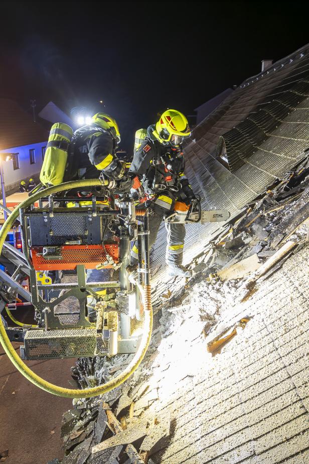 Zwei Feuerwehrmänner im Korb einer Drehleiter sowie am Dach, einer hält eine Motorsäge in Händen.
