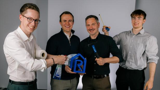 Vier Männer stehen nebeneinander, einer hält ein blaues Hausmodell mit einem "R" darauf, ein anderer eine blaue Sprühflasche, ein weiterer einen blauen Hammer, der vierte eine gelbe Wasserwaage.