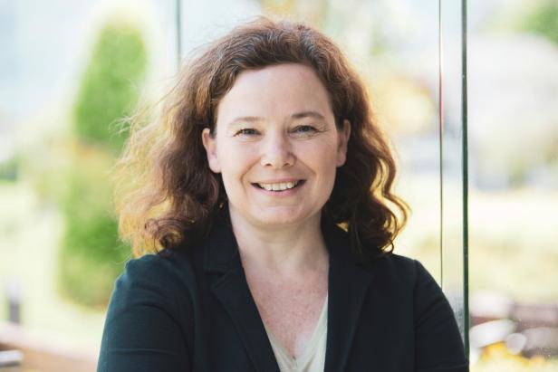 Frau mit lockigen Haaren und dunklem Blazer lacht in die Kamera