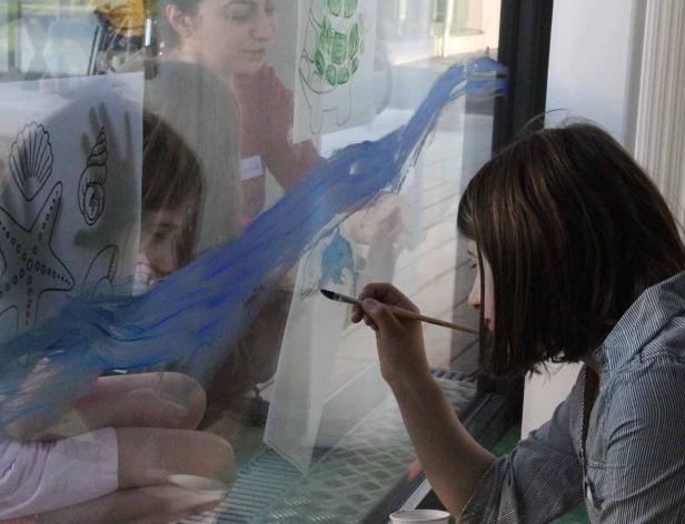 Eine Frau und ein Kind bemalen ein Fenster mit blauer Farbe.