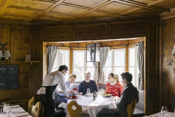 Mehrere Personen sitzen an einem runden Tisch in einem traditionellen Restaurant in Kitzbühel und werden von einer Servierkraft bedient.