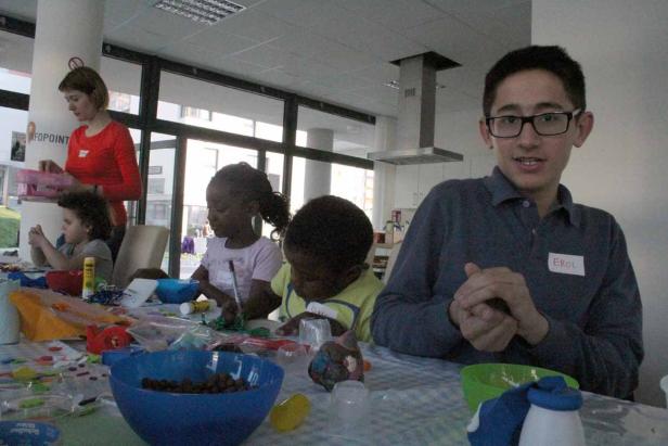 Kinder basteln mit einer Betreuerin an einem Tisch voller Materialien.