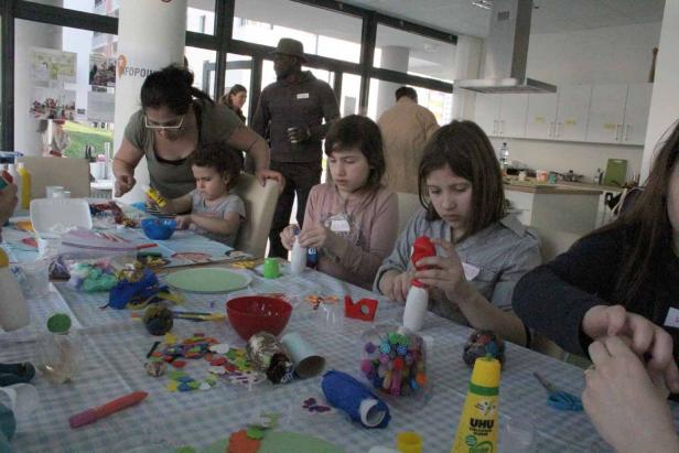 Kinder und Erwachsene basteln gemeinsam an einem Tisch mit verschiedenen Materialien.
