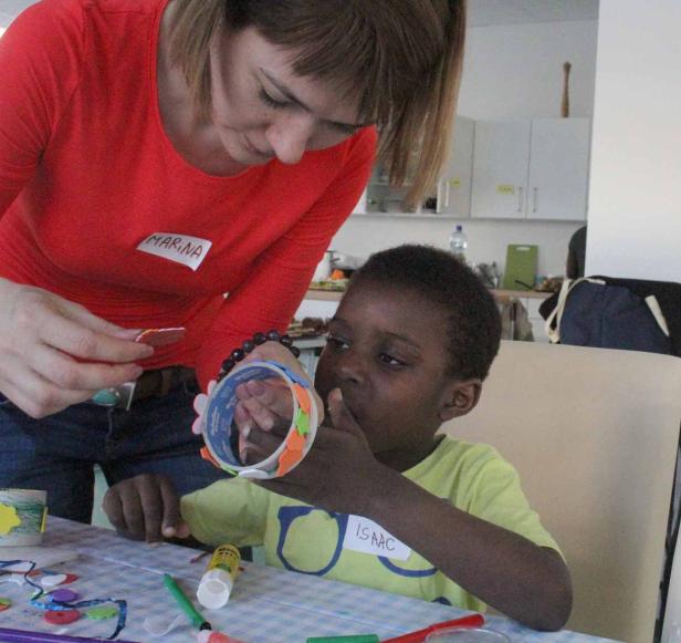 Marina hilft Isaac beim Basteln mit Papier und Klebstoff.