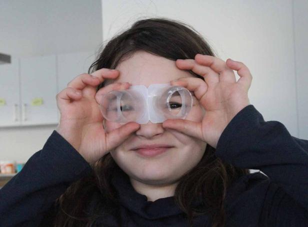 Ein Mädchen hält zwei leere Plastikbehälter vor ihre Augen wie eine Brille.