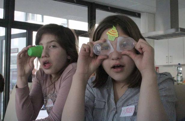 Zwei Mädchen spielen mit kleinen Plastikbechern vor ihren Augen.