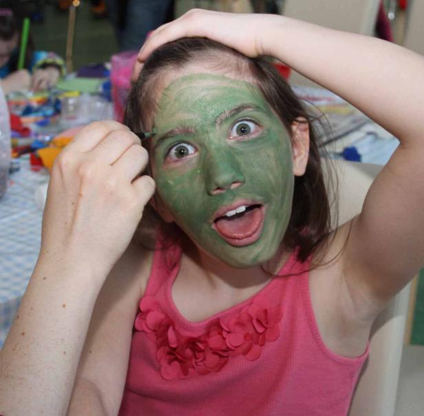 Ein Mädchen mit grüner Farbe im Gesicht schaut überrascht.