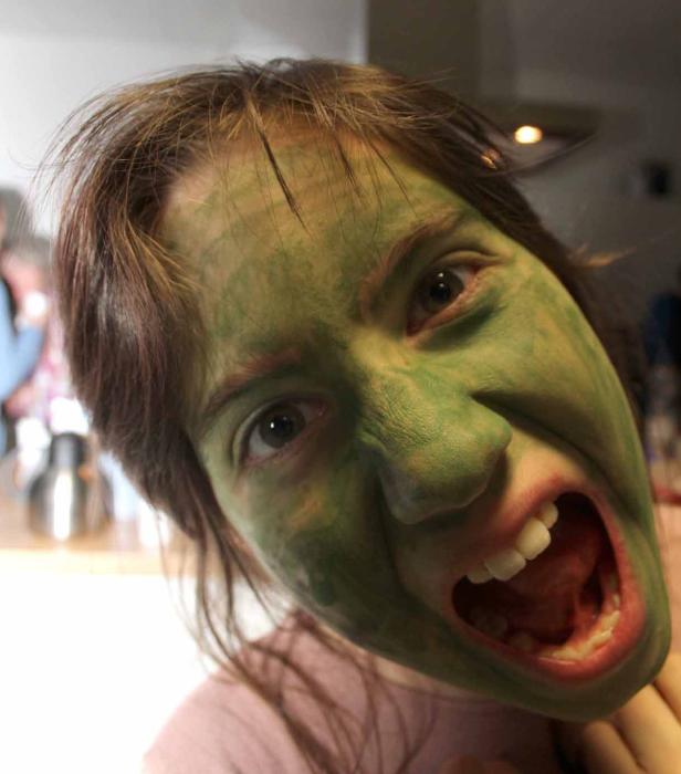 Eine Frau mit grün bemalten Gesicht schreit in die Kamera.