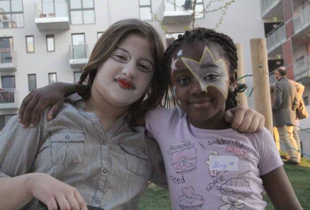 Zwei Mädchen mit Gesichtsbemalung umarmen sich vor einem Gebäude.
