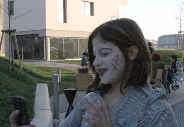 Ein Mädchen mit Gesichtsbemalung hält ein Smartphone in der Hand.