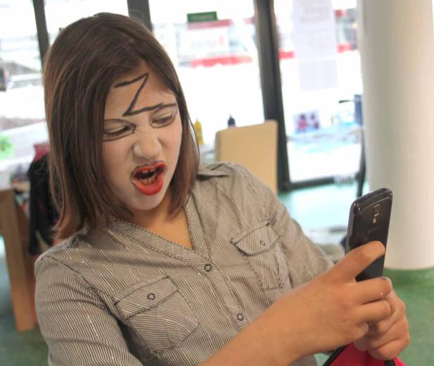 Ein Mädchen mit aufgemaltem Blitz auf der Stirn schaut grimmig auf ihr Handy.