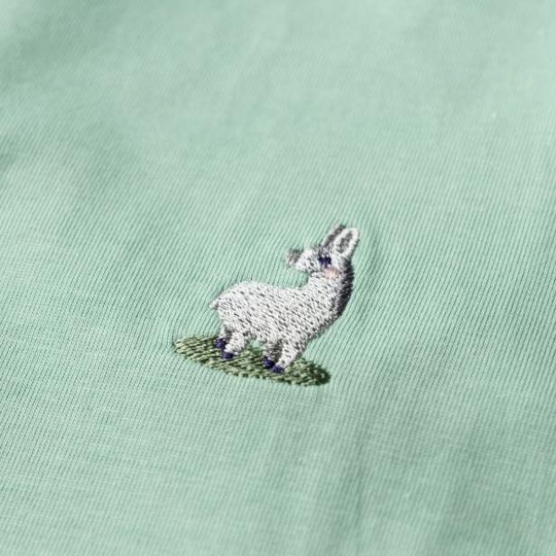 Stickerei eines weißen Esels mit schwarzen Hufen auf grünem T-Shirt.