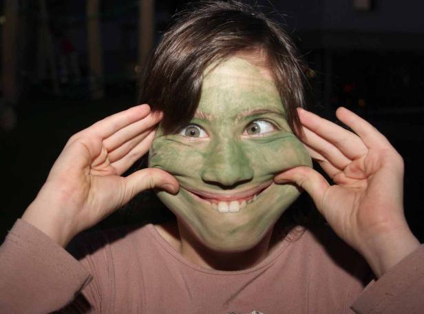 Eine Frau mit grüner Farbe im Gesicht zieht ihre Wangen auseinander.