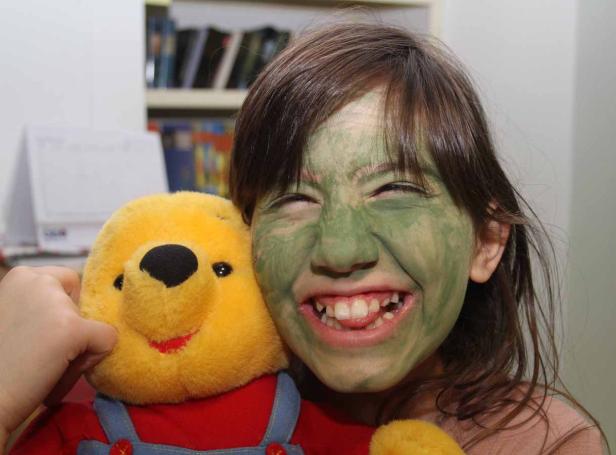 Ein Mädchen mit grüner Farbe im Gesicht umarmt einen Winnie Puh Bären.