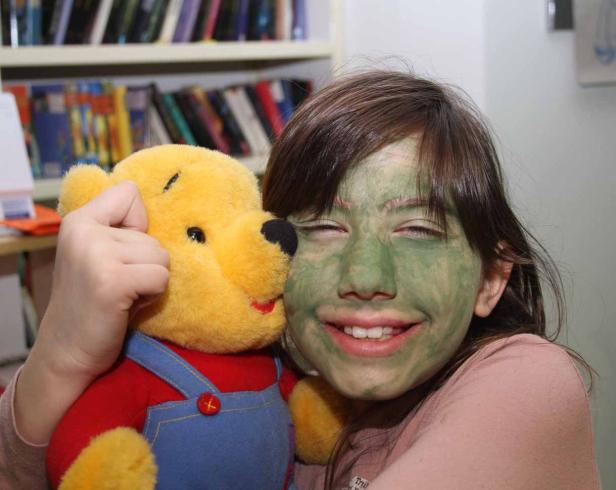 Ein Mädchen mit einer grünen Gesichtsmaske umarmt einen Winnie-the-Pooh-Teddybären.